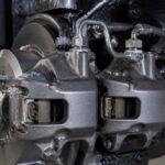 Dwa metalowe zaciski hamulcowe z przewodami hydraulicznymi przy tarczy samochodowej