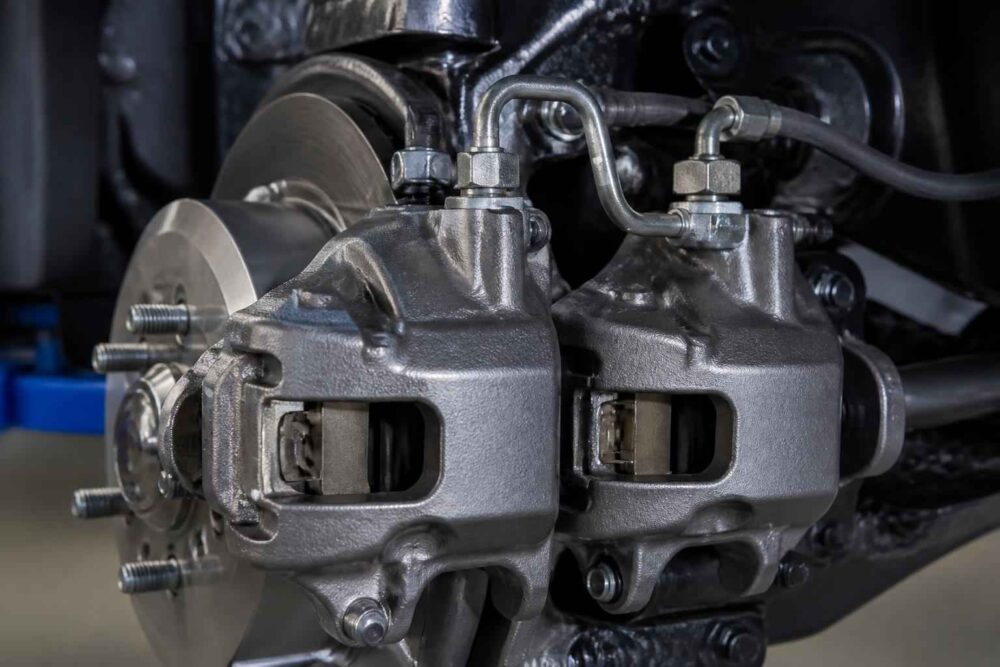Dwa metalowe zaciski hamulcowe z przewodami hydraulicznymi przy tarczy samochodowej